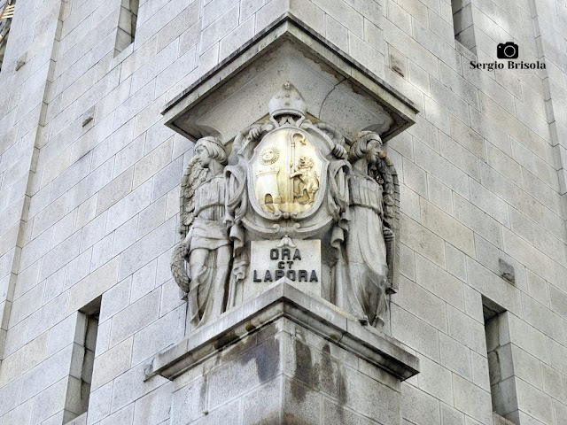 Close-up do Conjunto Escultórico Ora et Labora entre fachadas da Basílica Abacial Nossa Senhora da Assunção no Centro