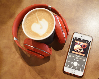 a brown table top with a pair of red Beats headphones surrounding a foamed coffee cup and next to them is an iPhone playing the audiobook The Mars Strain