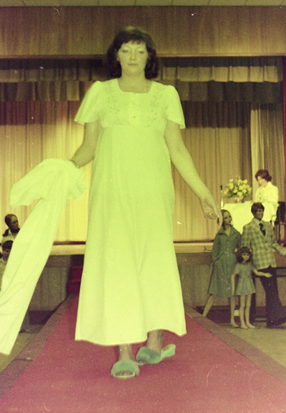 A staff member walking along a red carpet wearing a full-length white night dress and fluffy slippers