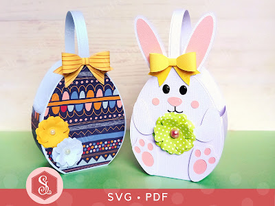 Two paper craft Easter baskets made in the shape of an egg and a white Easter bunny decorated with a paper bow and paper flowers