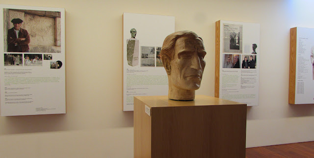 busto de Miguel Torga em Madeira e ao fundo vários painéis informativos
