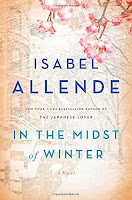 Book cover of In the Midst of Winter by Isabel Allende with a sepia-toned city block background and a cherry blossom tree branch in the foreground