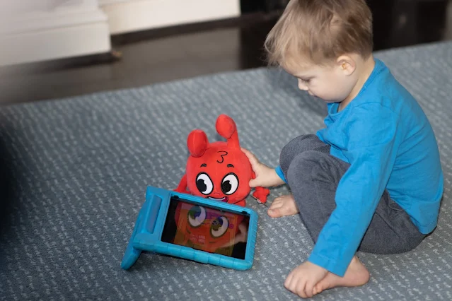 A boy sitting on the floor with an ipad with a Morphle plush reflected back on the screen