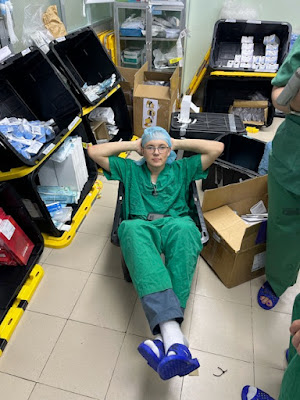 Young man in surgical scrubs sitting in a storage box.