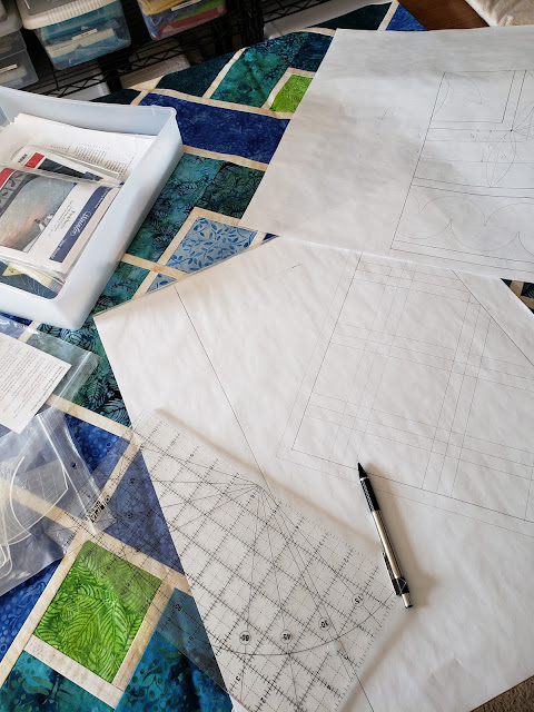 Paper, rulkers, templates and pencil strewn over a blue and green quilt top.  Quilting motifs are drawn on the paper.