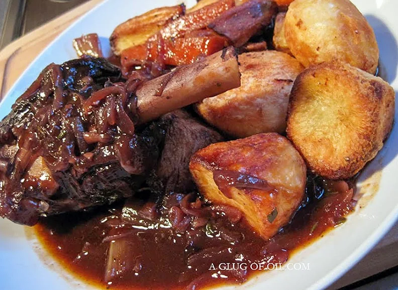 Braised lamb shanks recipe. Pictured on a plate with roast potatoes.