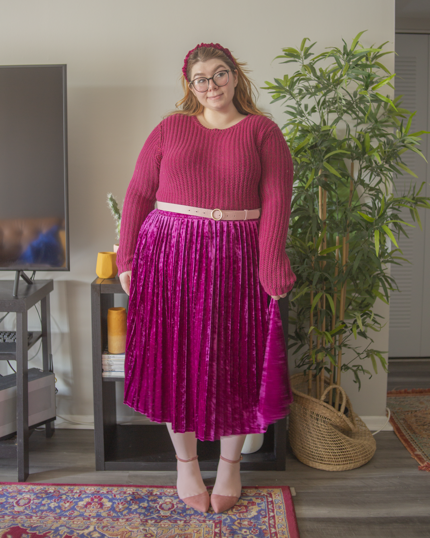 An outfit consisting of a berry colored cropped sweater, tucked into a berry colored velvet pleated midi skirt.