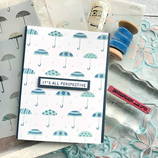 Rainy Day card made with : Scrapbook.com umbrellas stencil, pops of color snowflake, domed foam blending tool; Tim Holtz distress oxide speckled egg and faded jeans, tiny text stamp