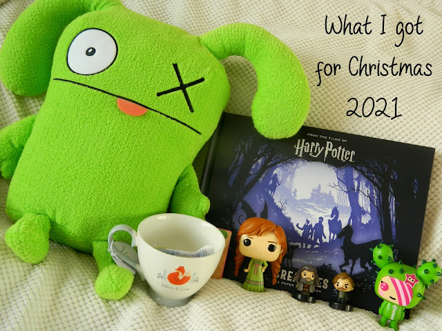 A photo showing Christmas presents that the blogger received: a harry potter book, a green monster plush, two funko pops (a cactus girl and Anna, a red-haired woman from Disney's Frozen), a mug with a fox on, and two tiny Harry Potter stamps of the characters Hagrid and Lupin.