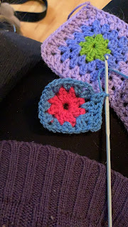 An in progress granny square. The center round is a bright midtone pink, and the second and  start of the third rounds are with a greyish blue.