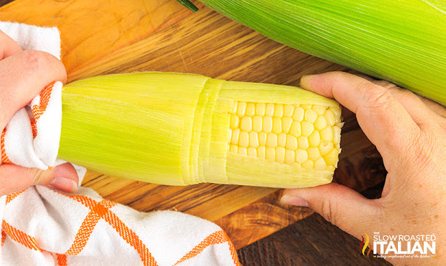 woman's hands holding ear of corn cooked in husk