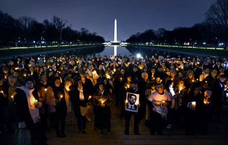 a crowd of people holding candles and photos of Bijan in the dark