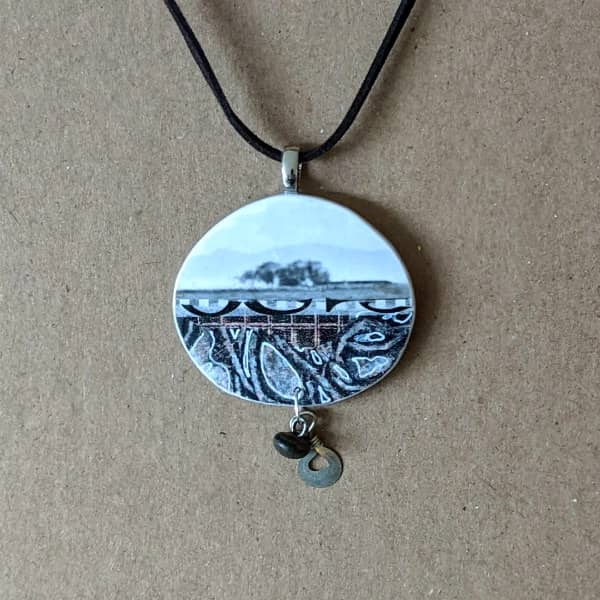 handmade round collage pendant in shades of blue-grey with dangling charms and black necklace cord