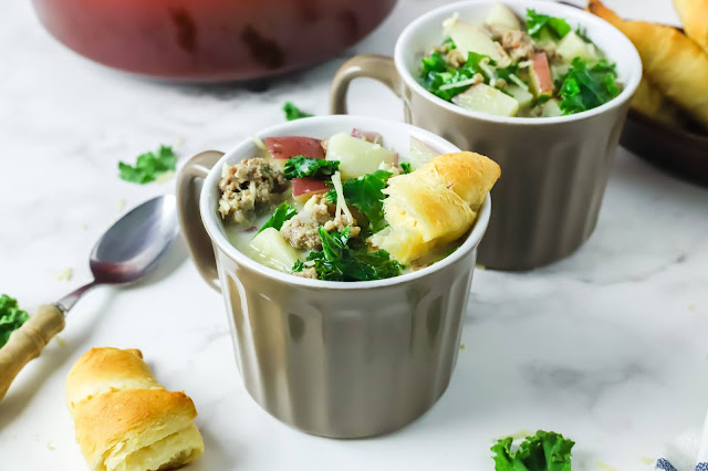 Cups of soup with spoons and bread rolls.