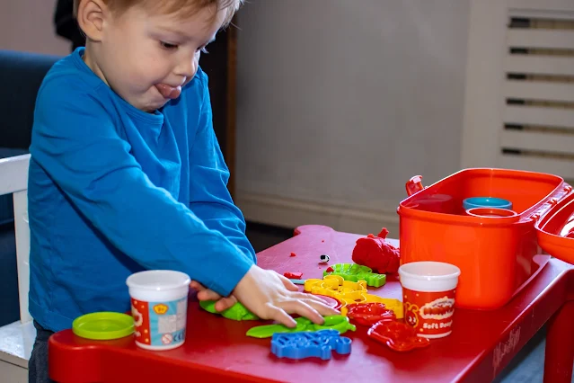 a toddler with the Morphle dough set contents on a red table using a green cookie cutter