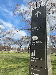 Photo of a pillar in front of a green lawn showing directions to the Smithsonian Metro, Freer Gallery of Art, Smithsonian Castle, and more.