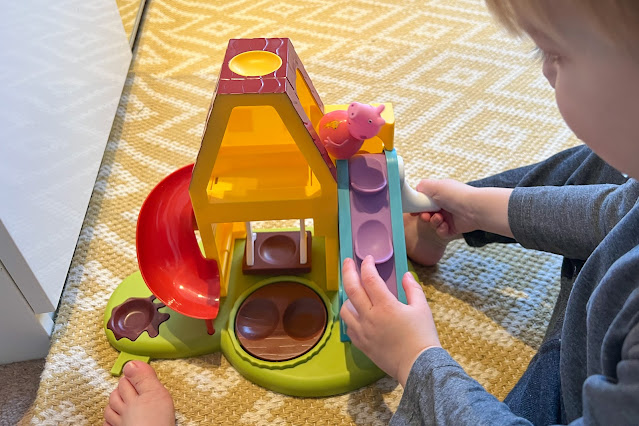 A toddler winding a lever to make Peppa Pig Weeble go up the moving stairs and on to a platform at the top