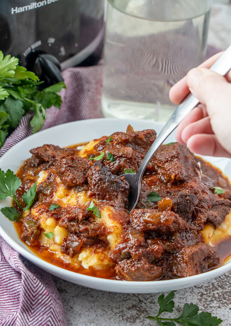 spoon in a bowl of beef with mashed potatoes.