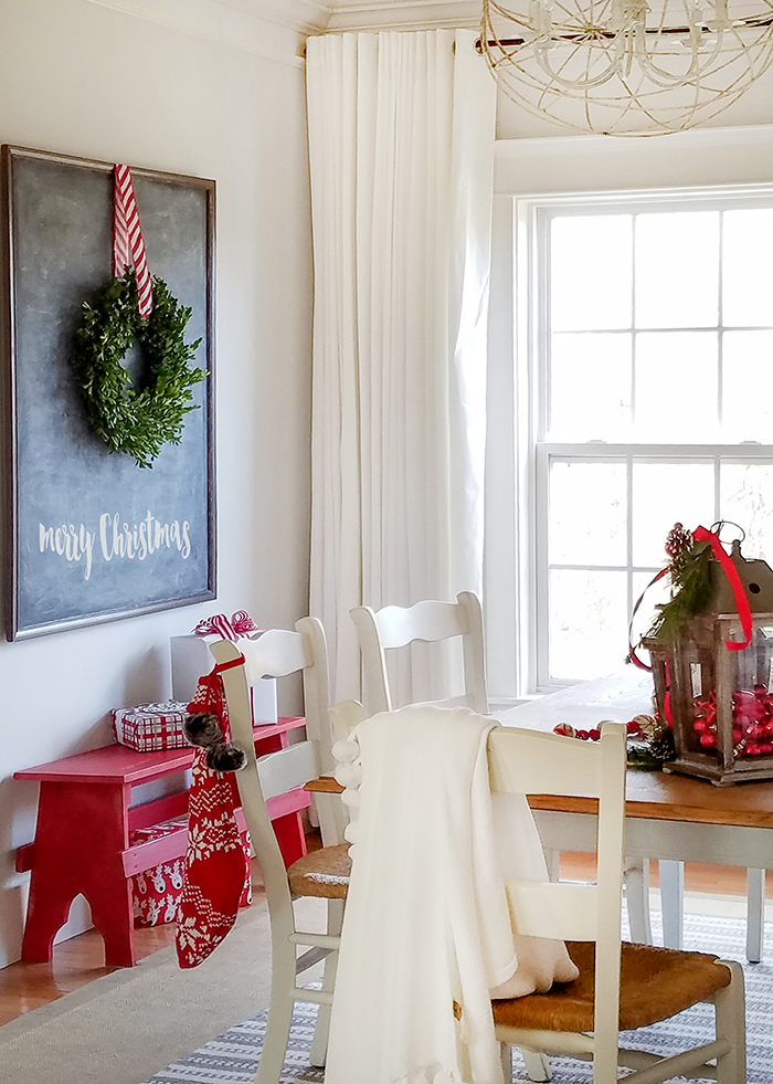 Chalkboard holding a boxwood wreath a top a red bench with dining table in front.