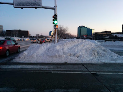 Pedestrian activation button on a pole surrounded by huge pile of snow on a porkchop island