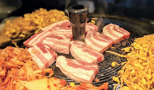 Uncooked slices of thick 삼겹살 Samgyupsal (pork belly) placed on grill