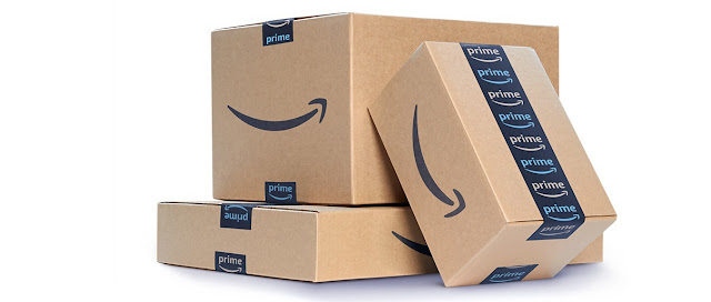 Imagem meramente ilustrativa: uma pilha de caixas de papelão, fechadas comfita adesiva preta com a logo da Amazon. Fundo branco.