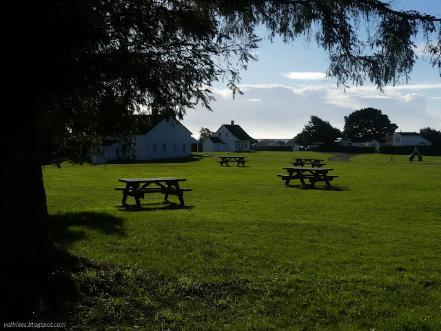 00: well grassy field with picnic tables and white buildings at the edges