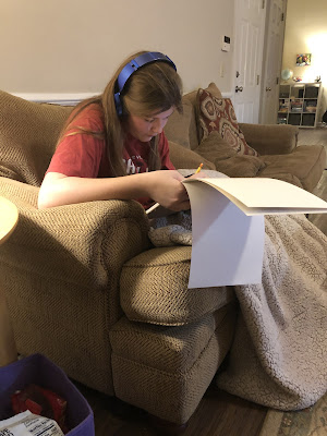 Elizabeth sitting on the family room couch with headphones on drawing.