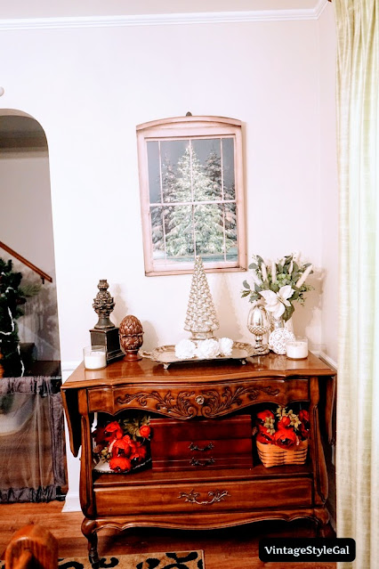 Buffet with Christmas decor on top with snowy tree picture on wall