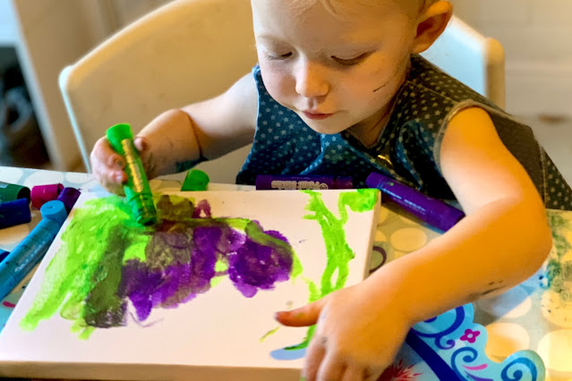 A preschooler painting a canvas using paint sticks making less mess that with normal mess