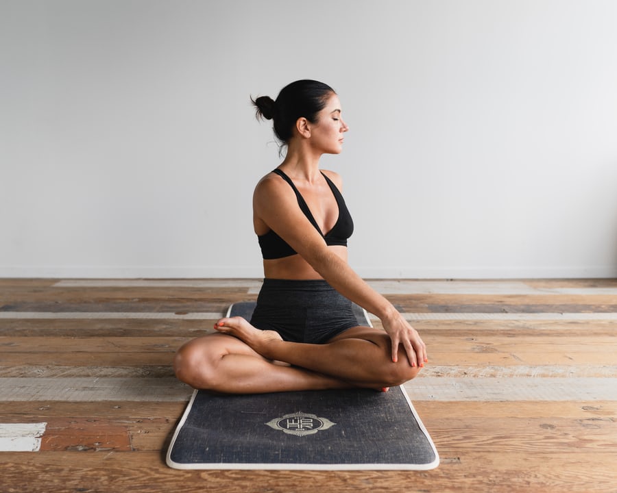 A fitness woman in black training gear stretching while sitting on a black mat to lose weight