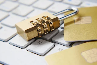 A coded padlock on a white laptop keyboard near a gold credit card.