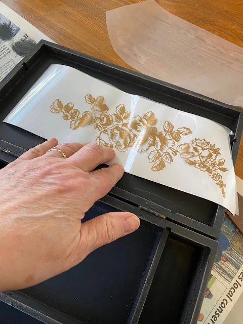 Photo of gold floral decor transfers from Redesign With Prima being added to a vintage artist case.