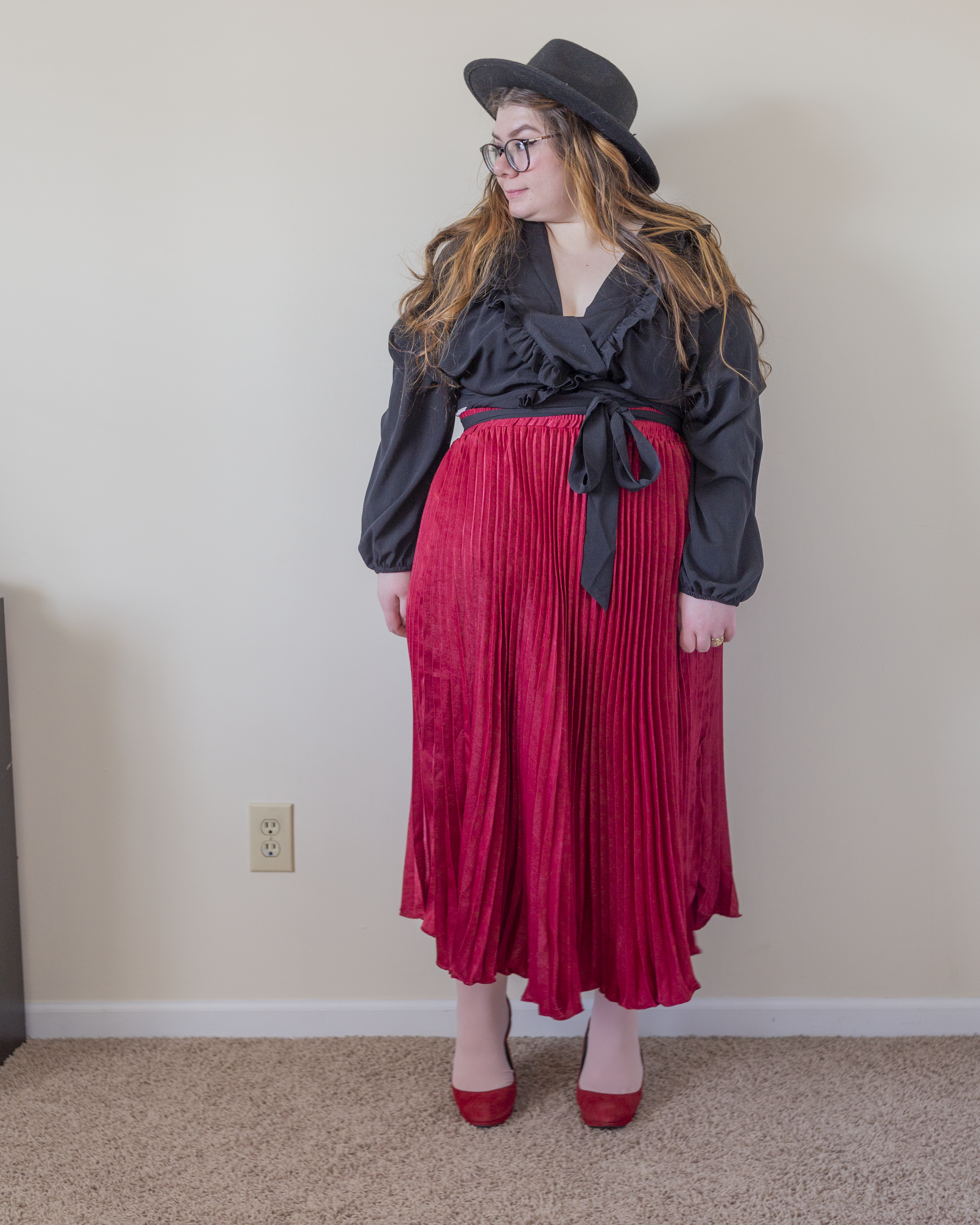 An outfit consisting of a black wrap top with a ruffle bodice, a wine red pleated maxi skirt, and red round toe slingback heels.