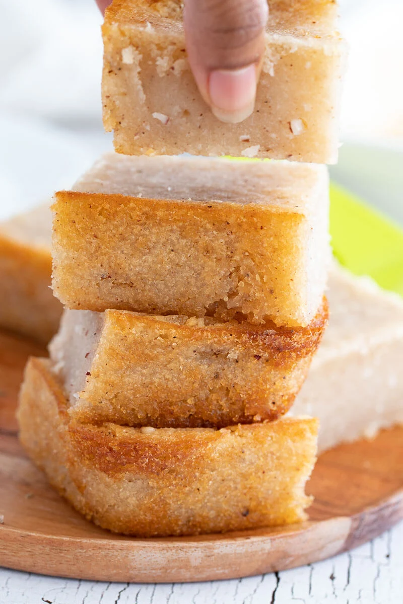 A stack of cassava pone slices with a hand holding the top slice.