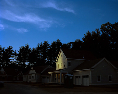 a house is seen in dim light besides trees and open sky