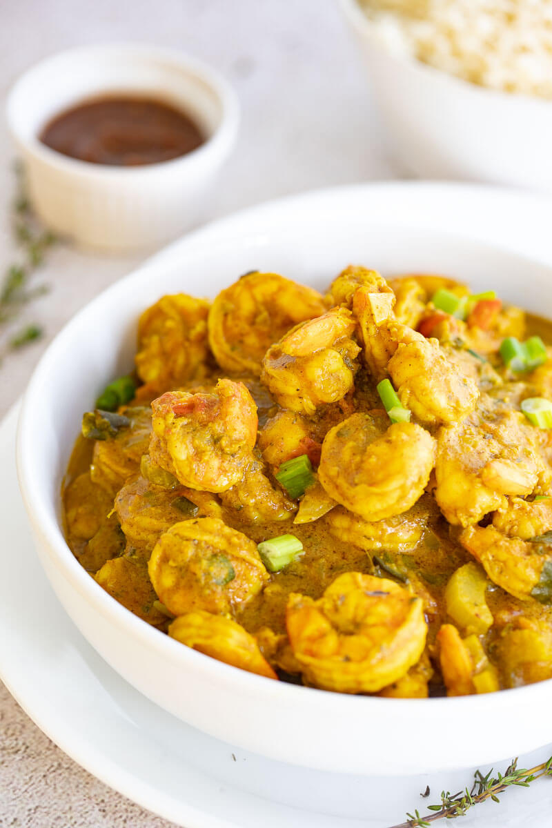 A large white bowl of curry shrimp with a small bowl of tamarind sauce in the back.