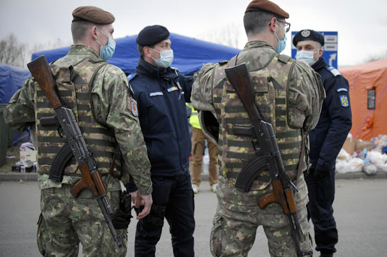 Armed Military Police converse with gendarmes as they observe refugees fleeing the violence in neighboring Ukraine at the Romanian-Ukrainian border in Siret, Romania, on Sunday, February 27, 2022. Concerns are developing about how to safeguard the most vulnerable migrants from being targeted by human traffickers or becoming victims of other sorts of exploitation as millions of women and children escape over Ukraine's borders in response to Russian aggression. Image Credit: (AP Photo/Andreea Alexandru)