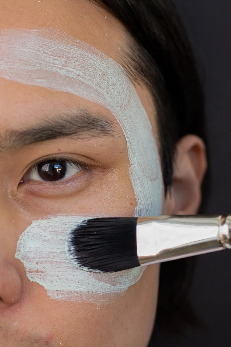 woman applies mask onto her face with a synthetic brush