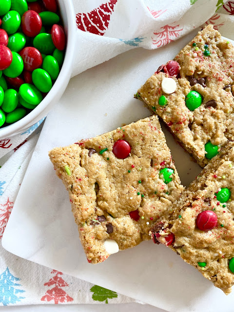 Monster cookie bars plated by a bowl of holiday M&M's