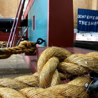 Close-up of a coil of rope in Erie Maritime Museum exhibit. Blue banner with white letters in background says "Don't Give Up the Ship"