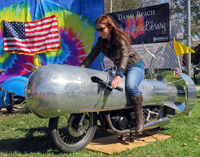 Woman astride rocket shaped motorcycle.