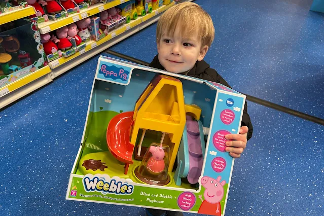 A toddler holding Peppa Pig Weebles play set in Smyths about to buy it