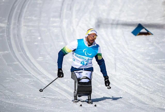 Robelson usando um esqui adaptado com uma cadeira. O brasileiro usa um agasalho azul e branco com um colete com o número 42 por cima