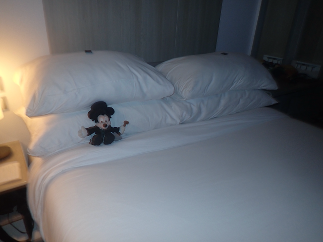 Gravedigger Mickey plushie on a bed that has been turned down for the evening.