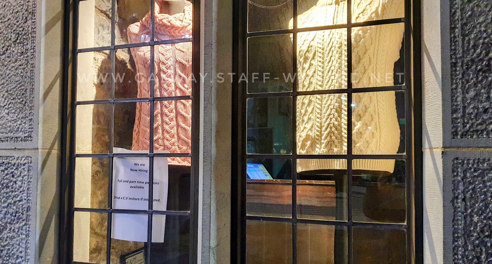 pink and white aran knit sweaters in a leaded glass window, with a staff-wanted advertisement