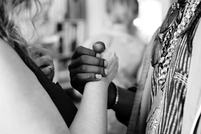 A picture is shown at chest level. A white person and an African shake hands, and held over their hearts.