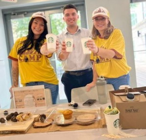 woman , man, and woman standing behind table holding Starbucks cups