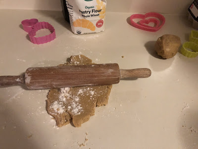 Some cookie dough, a rolling pin, and some cookie cutters on the counter.