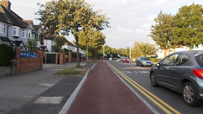 A road with red cycle tracks, then verges with trees and footways at the back.